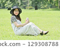 A young woman sitting on the grass and taking a break drinking water from a water bottle 129308788