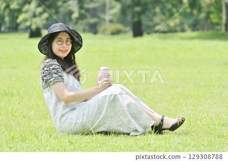 A young woman sitting on the grass and taking a break drinking water from a water bottle 129308788