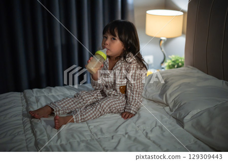 toddler baby girl drinking milk from bottle on a bed at night toddler baby girl drinking milk from bottle on a bed at night 129309443