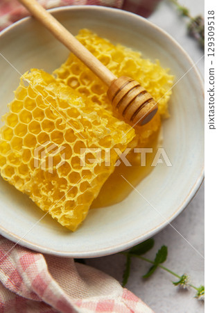 Honeycomb and honey dipper resting in bowl on table 129309518