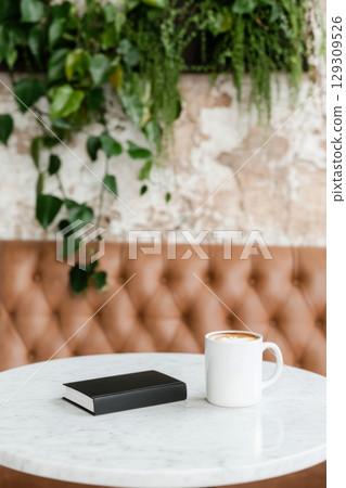 Coffee cup and notebook on round marble table with plant background 129309526