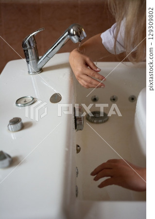 Detail shot of a woman testing water temperature at a tub faucet, showcasing relaxation and self-care in a bathroom setting. 129309802