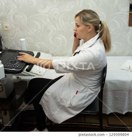 Doctor on phone using medical machine, white coat, diagnostic equipment. Medical call center employee in the doctor's office working. Doctor on phone using medical machine, white coat, diagnostic equipment. Medical call center employee in the doctor's office working. 129309804
