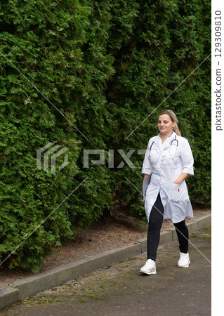 Medical professional walking outdoors with stethoscope and lab coat. Healthy lifestyle, nature and healthcare concept. 129309810