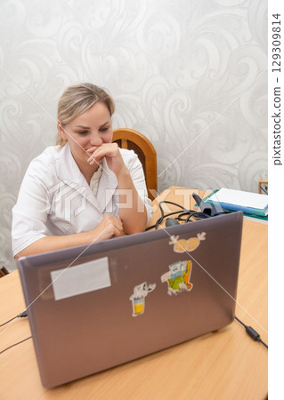 Doctor engaging in telemedicine consultation, providing medical care remotely with smile. Video conference shows screen and stickers. Doctor engaging in telemedicine consultation, providing medical care remotely with smile. Video conference shows screen and stickers. 129309814