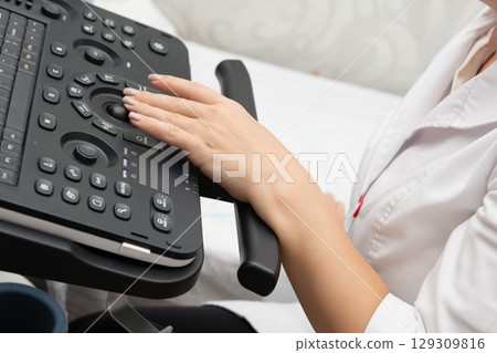 Close-up of a medical professional operating an ultrasound machine, displaying precision and control during a diagnostic procedure. Close-up of a medical professional operating an ultrasound machine, displaying precision and control during a diagnostic procedure. 129309816