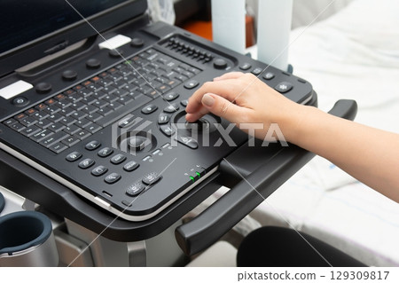 Medical professional operating diagnostic ultrasound equipment. Image shows detailed keyboard and control panel in clinical environment. 129309817