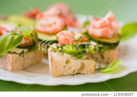 Delicious portioned appetizers with shrimps and greens on a green background Delicious portioned appetizers with shrimps and greens on a green background 129309897