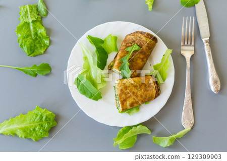 Appetizing omelette with greens and arugula on a white plate 129309903