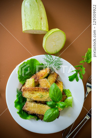 Homemade fried zucchini on a white plate on a brown background 129309922