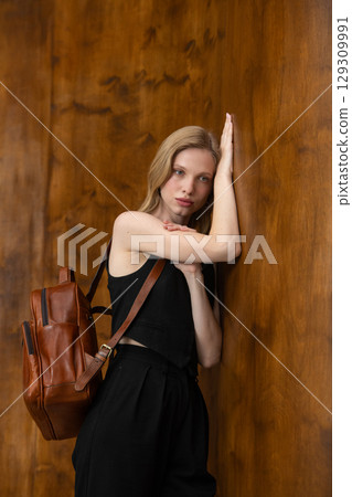 A fashion model is captured from a back-facing perspective, holding a rich brown leather backpack and looking away, showcasing the product in a minimalist setting. A fashion model is captured from a back-facing perspective, holding a rich brown leather backpack and looking away, showcasing the product in a minimalist setting. 129309991