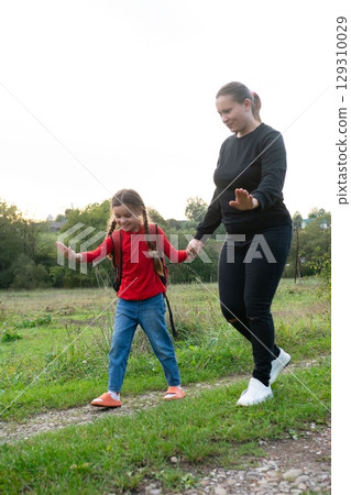A mother and daughter stroll hand-in-hand along a rural path, enjoying a peaceful moment in nature. A mother and daughter stroll hand-in-hand along a rural path, enjoying a peaceful moment in nature. 129310029
