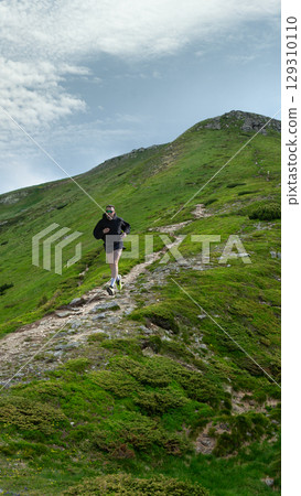 Bold poster of man in black running uphill on winding rocky mountain path in green landscape Bold poster of man in black running uphill on winding rocky mountain path in green landscape 129310110