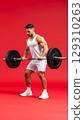 Muscular man in white athletic wear lifting heavy barbell with focused expression on red background 129310263