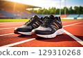 Pair of black and gray running shoes with orange accents placed red running track warm sunlight, evoking energy and readiness 129310268