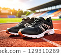 Pair of black running shoes with white soles on red track at stadium during sunset, ready for exercise 129310269