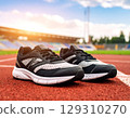 Pair of black and white running shoes placed on red track with blurred stadium background and warm sunlight shining 129310270