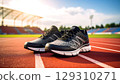 Pair of black and gray running shoes placed red outdoor track with stadium and blue sky background, evoking energy 129310271