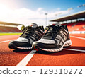 Pair of black and white running shoes placed on red outdoor track under bright sunlight, ready for exercise 129310272