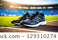 Pair of blue and black running shoes placed on track with blurred stadium background, evoking energy and readiness for sport 129310274