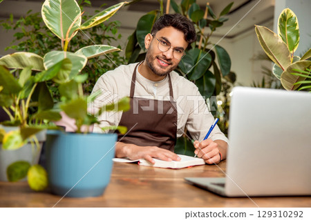 Young man sitting at the laptop in the flower shop Young man sitting at the laptop in the flower shop 129310292