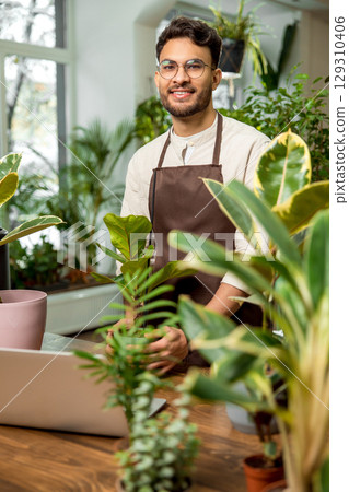 Young man in eyeglasses in the flower shop looking contented and smiling 129310406