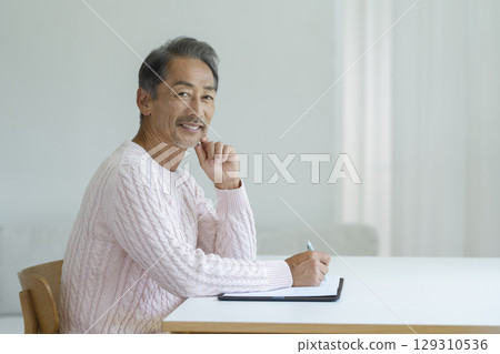 Senior man looking at camera and smiling while holding a pen 129310536