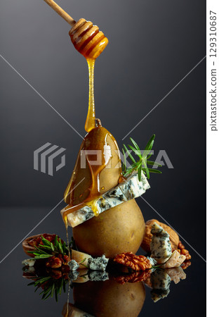 Blue cheese with honey, pear, walnuts, and rosemary on a black background. 129310687
