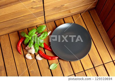 Empty black plate, garlic, basil, and red pepper on a natural wooden background. 129310694