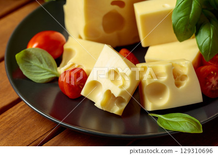Swiss cheese, green basil, salad, and tomatoes on a wooden table. Swiss cheese, green basil, salad, and tomatoes on a wooden table. 129310696