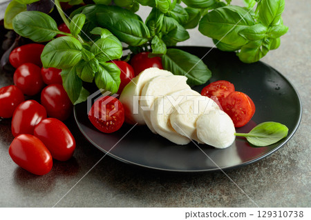 Mozzarella cheese with cherry tomatoes and basil on a stone table. 129310738