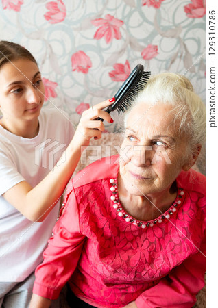 Care and connection shine in a moment shared between a young girl and her grandmother in a cozy living room filled with warmth and love during a sunny afternoon 129310786
