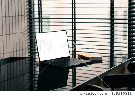 Modern workspace with laptop and book on sleek black table near window blinds in a stylish office 129310811