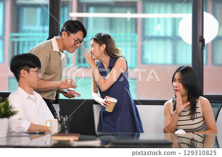 Young office workers engaging in private conversations, sharing secrets and gossip during work hours 129310825