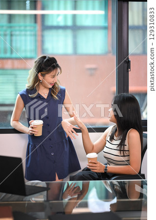 Two female office workers chatting by the window during a coffee break 129310833