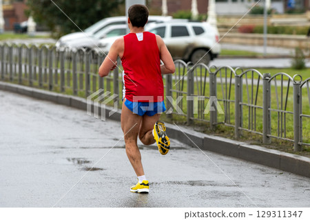 rear view runner running marathon on wet road, splashing mud on his legs rear view runner running marathon on wet road, splashing mud on his legs 129311347