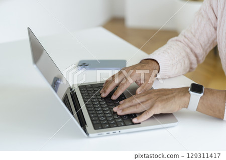 一位 60 多歲男士的手正在使用筆記型電腦 一位 60 多歲男士的手正在使用筆記型電腦 129311417