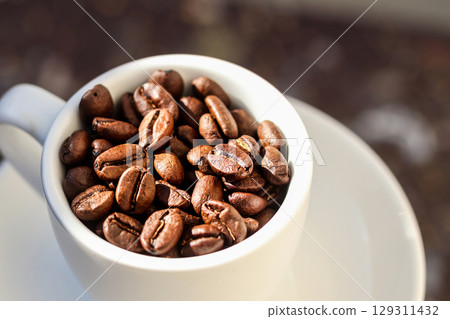 A beautiful close-up of roasted coffee beans scattered around a clean, white cup. The intricate grain and texture of the beans create a stunning pattern on a simple background A beautiful close-up of roasted coffee beans scattered around a clean, white cup. The intricate grain and texture of the beans create a stunning pattern on a simple background 129311432