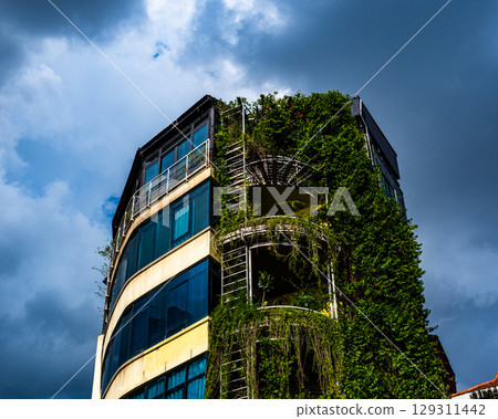 Modern urban building covered in lush green ivy under dramatic sky_Hanoi, Vietnam Modern urban building covered in lush green ivy under dramatic sky_Hanoi, Vietnam 129311442