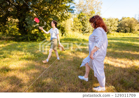 Caucasian woman and daughter throw frisbee in a natural green park area. Concept of vacation time, fitness, parenting and outdoor family entertainment. 129311709