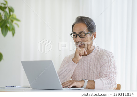 A man in his 60s wearing earphones in front of a laptop A man in his 60s wearing earphones in front of a laptop 129311834