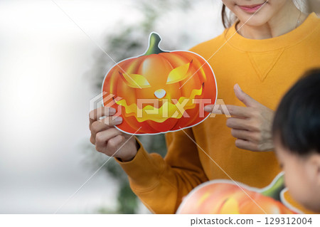 Halloween Fun. Child holding a playful pumpkin mask during festive activities. 129312004