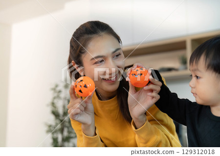 Halloween Celebration. Mother and child enjoying festive activities with pumpkin decorations. 129312018