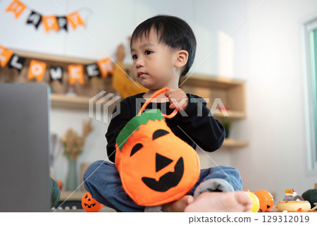 Halloween Fun. Young child holding a pumpkin bag, ready for trick-or-treating in a festive home. Halloween Fun. Young child holding a pumpkin bag, ready for trick-or-treating in a festive home. 129312019