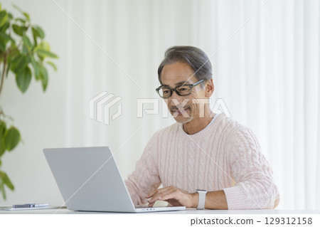 一位 60 多歲的男子正在使用筆記型電腦 129312158