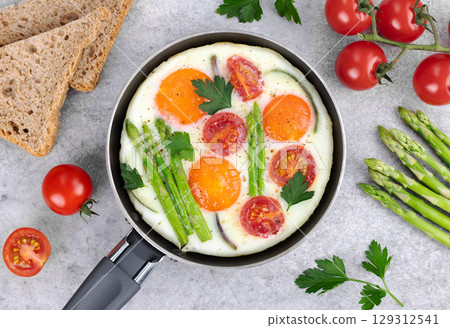 Fried eggs with vegetables asparagus, tomatoes and onions, toasts on a gray wooden background. Top view. Breakfast food. Fried eggs with vegetables asparagus, tomatoes and onions, toasts on a gray wooden background. Top view. Breakfast food. 129312541