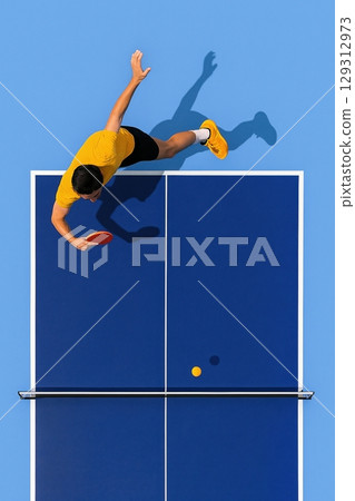 Table tennis player in yellow outfit serving ball on blue court from top-down view 129312973