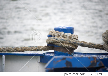 Close-Up of Nautical Rope Secured on a Blue Post by the Water 129312998
