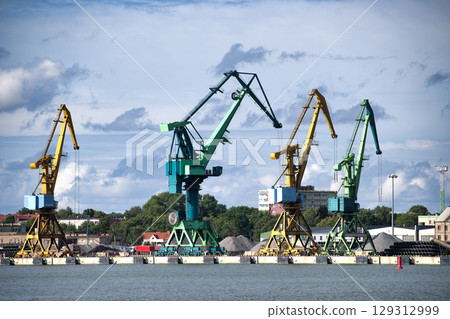 Colorful cranes stand tall in a busy port under a dramatic, cloudy sky. Colorful cranes stand tall in a busy port under a dramatic, cloudy sky. 129312999