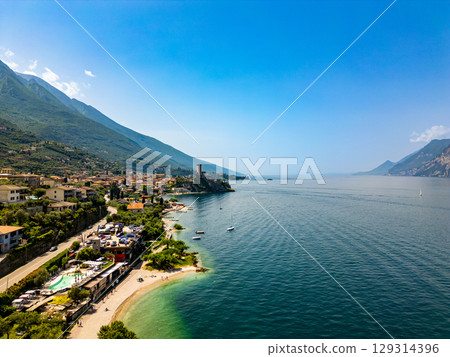 Drone aerial view of Malcesine town and lake Garda coastline. View of beach and the medieval castle above city. Drone aerial view of Malcesine town and lake Garda coastline. View of beach and the medieval castle above city. 129314396